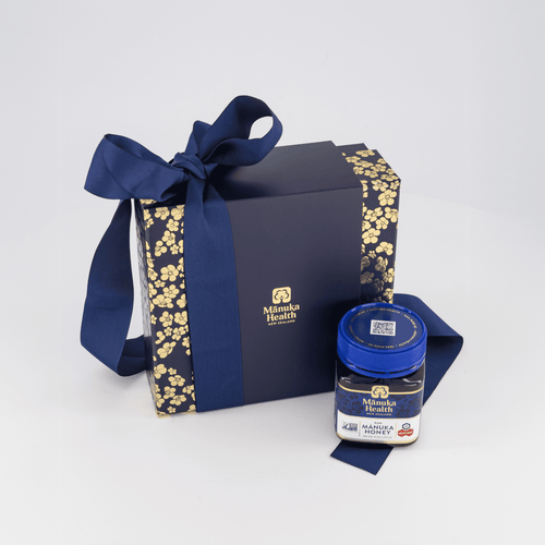 Manuka Health gift set with MGO 400+ honey and wooden spoon in a decorative box with a bow on a white background.