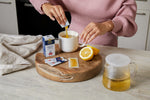 Person making a cup of tea with lemon and honey on a wooden cutting board.