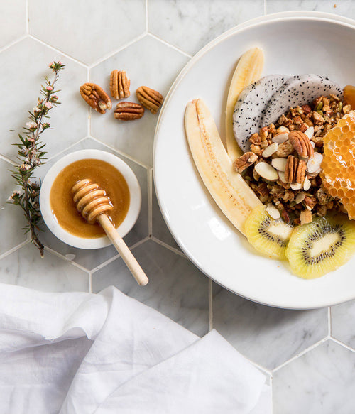 Fruit and granola bowl with honey on a marble surface.