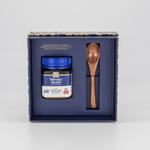 Manuka Health gift set with MGO 400+ honey jar with a wooden spoon in a decorative box on a light gray background.