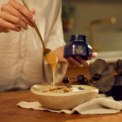 Person pouring a spoonful of Manuka Health manuka honey into a bowl of yogurt.