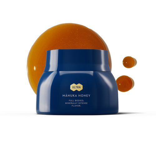 Blue jar of Ultra Manuka Honey with honey drips on a white background.