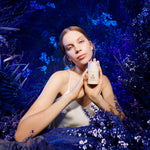 Woman holding a skincare product in a mystical forest setting for Manuka Health. 